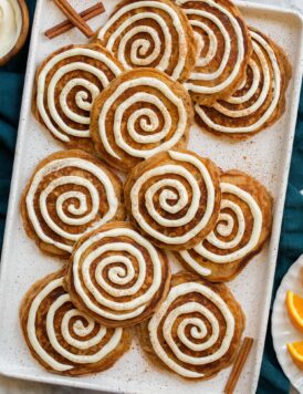 Cinnamon roll pancakes shown featuring cinnamon pancakes with a cream cheese swirl over pancakes. They are all laid out on a platter and shown from overhead.
