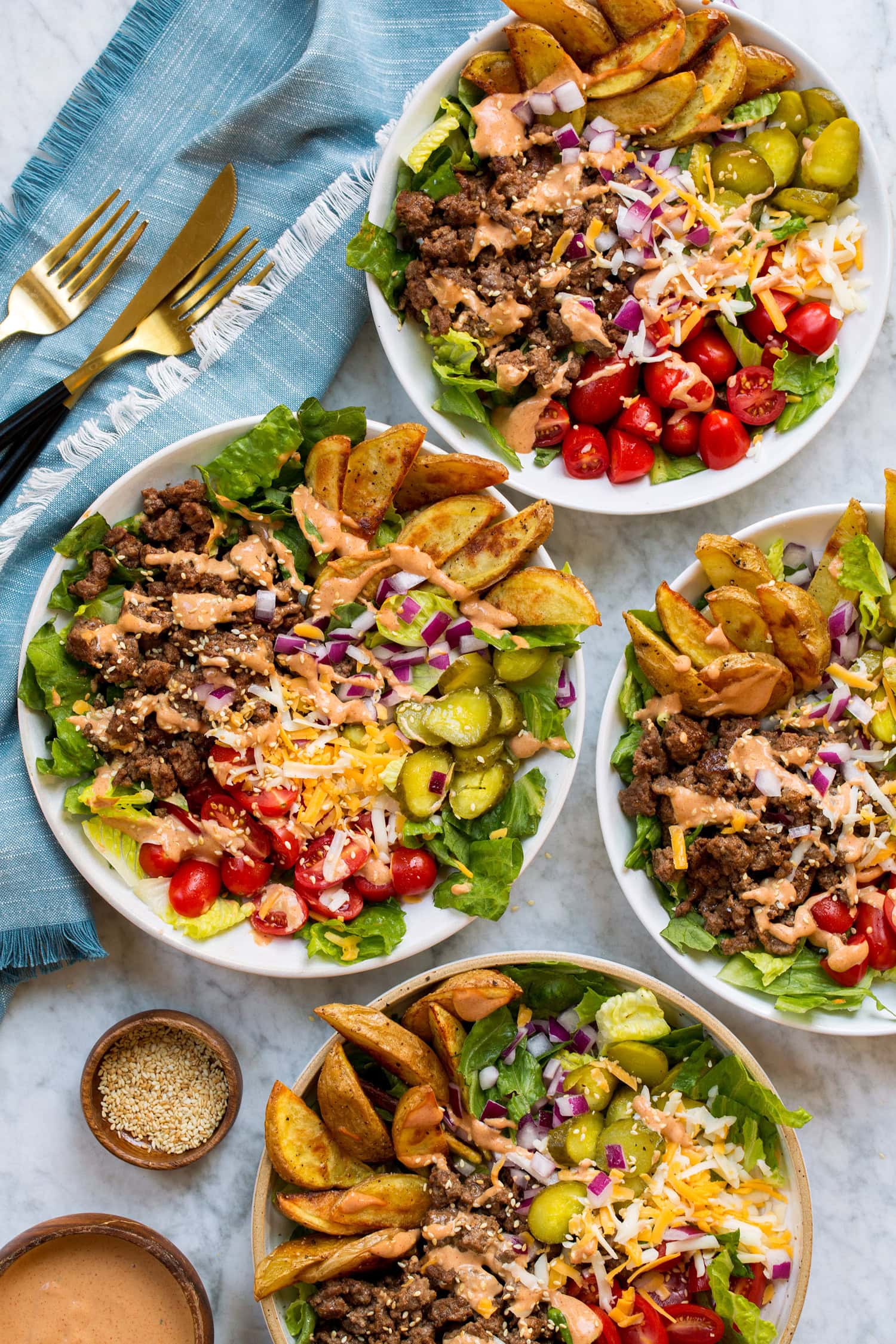 Burger Bowls Four burger bowls shown from overhead on a marble surface with a blue cloth to the side.