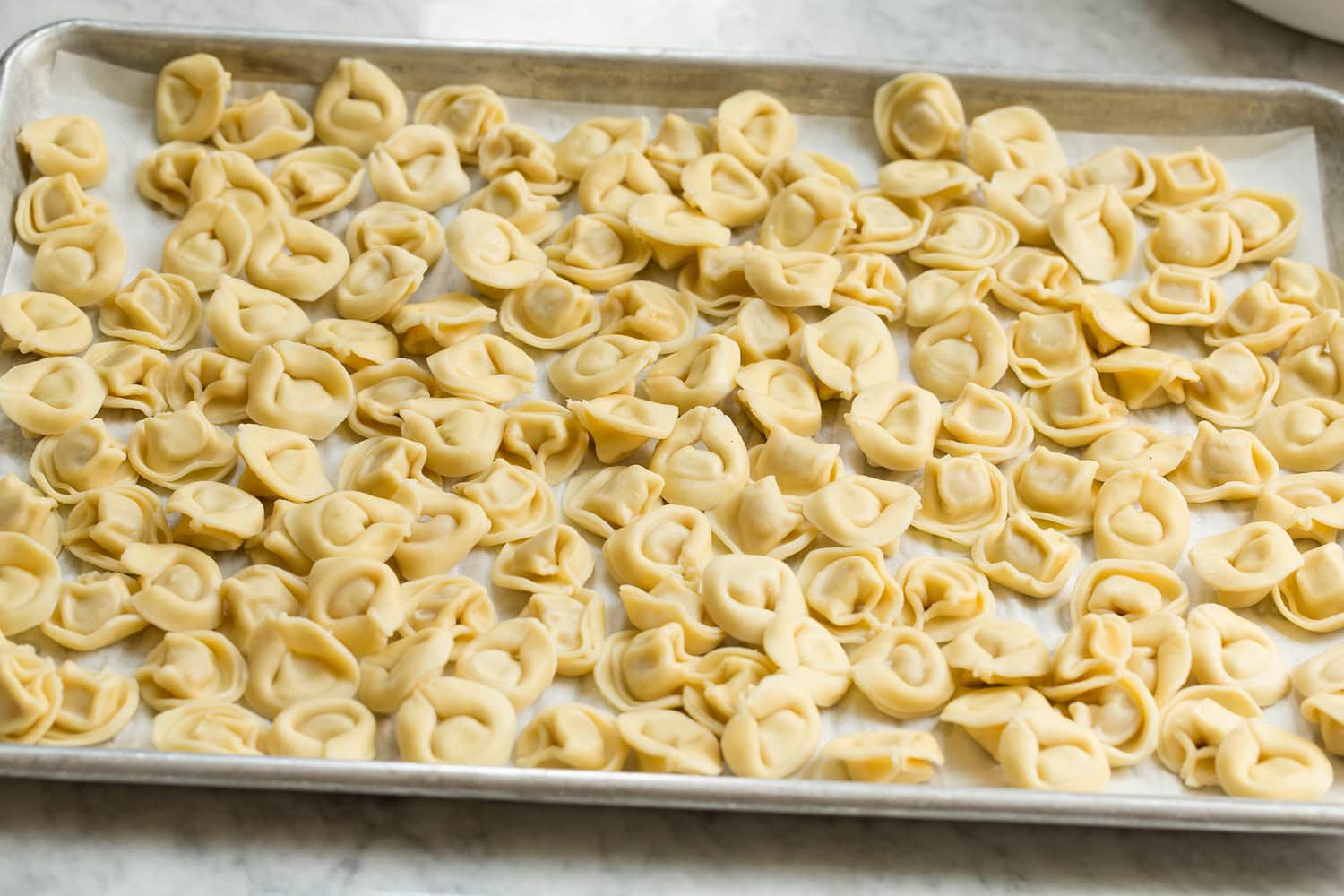 Tortellini Pasta Salad Tortellini pasta salad cooling on a baking sheet.