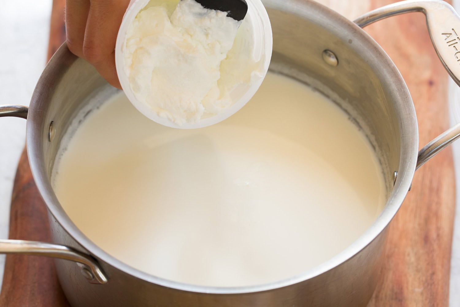 Homemade Yogurt Adding greek yogurt to milk in pot.