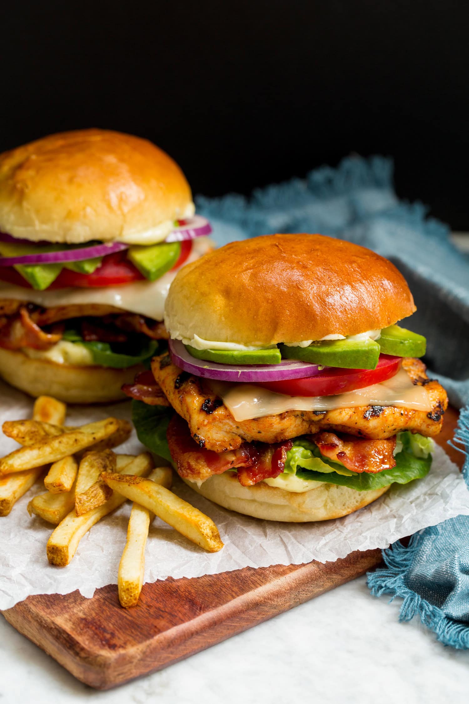 Grilled Chicken Sandwich layered with grilled chicken breast, lettuce, bacon, cheese, tomato, avocado, ranch mayo and buns.