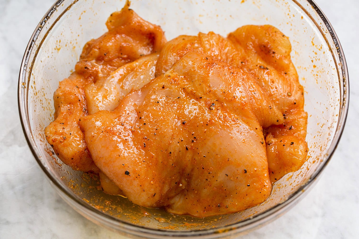 Grilled Chicken Sandwiches Chicken breasts tossed with seasoning in a glass mixing bowl.