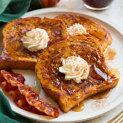 Three slices of homemade pumpkin french toast with maple syrup and whipped cream swirled on top.