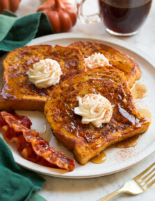 Three slices of homemade pumpkin french toast with maple syrup and whipped cream swirled on top.