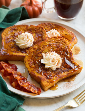 Three slices of homemade pumpkin french toast with maple syrup and whipped cream swirled on top.