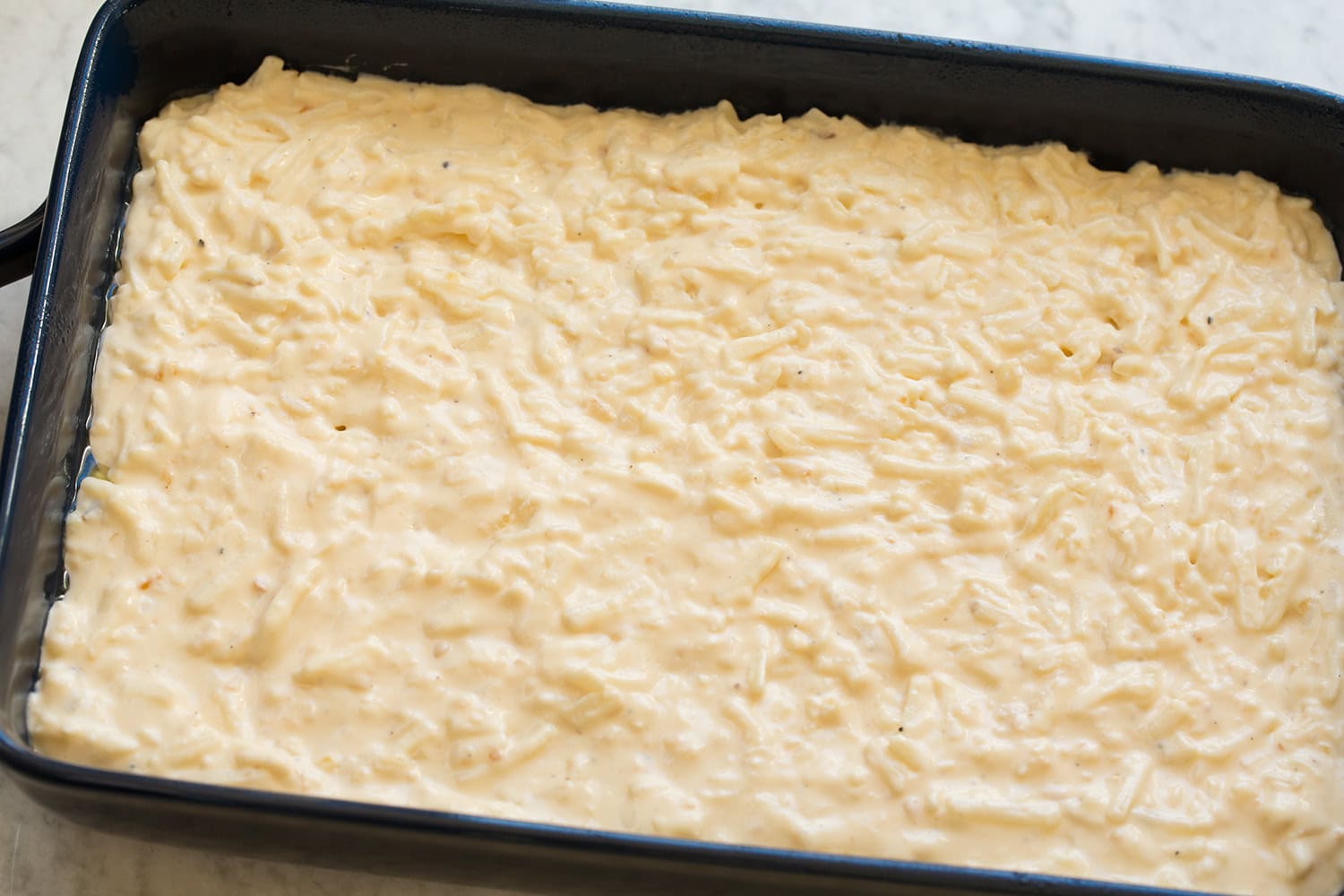Funeral Potatoes Sauce coated hash browns spread out even in a baking dish.