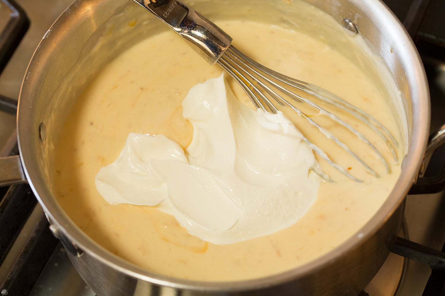 Funeral Potatoes Sour cream added to sauce in saucepan.