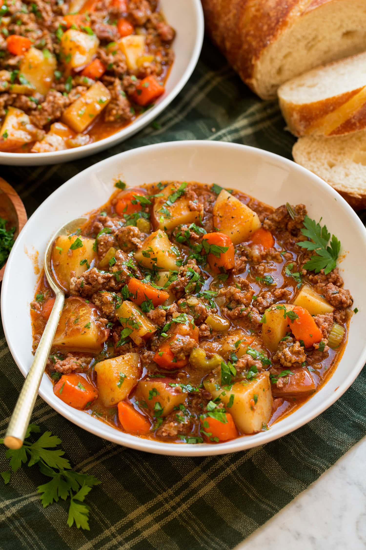 Slow Cooker Ground Beef Stew Ground beef stew shown in a white serving bowl over a green plaid cloth.