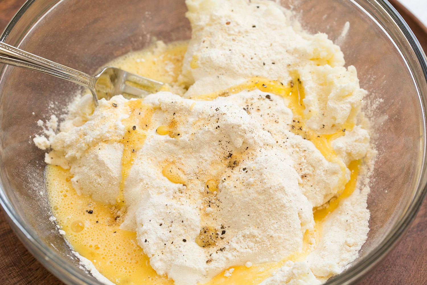 Mashed Potato Cakes Potato cake mixture with flour and eggs shown before mixing in a glass mixing bowl.