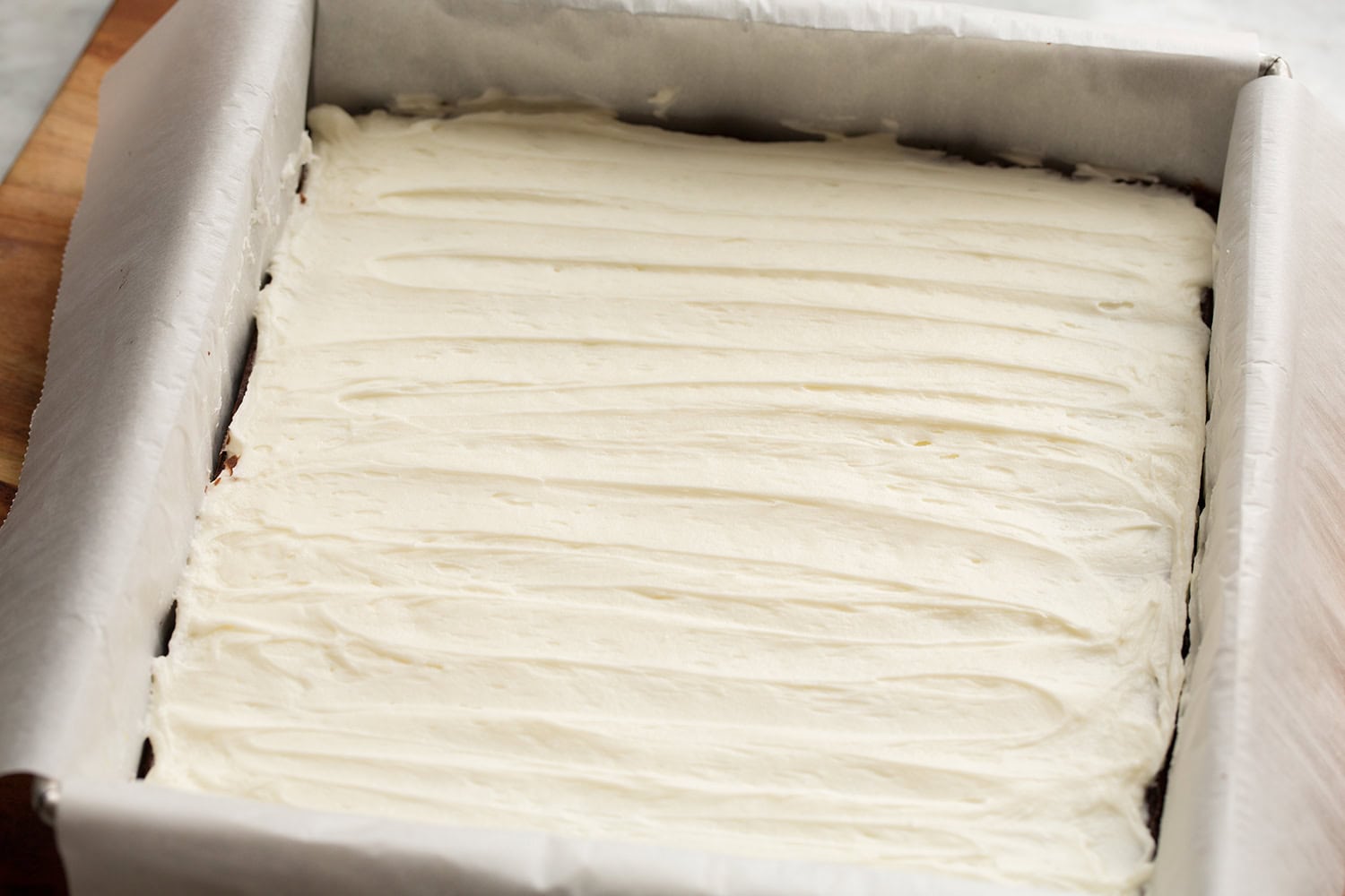 Peppermint frosting spread atop brownies in baking pan.