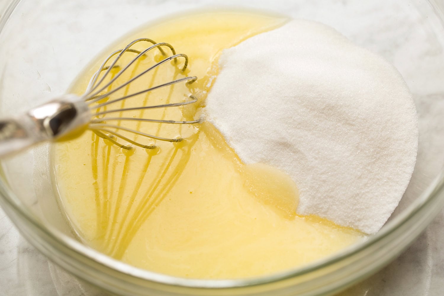 Whisking melted butter and sugar in a glass mixing bowl.