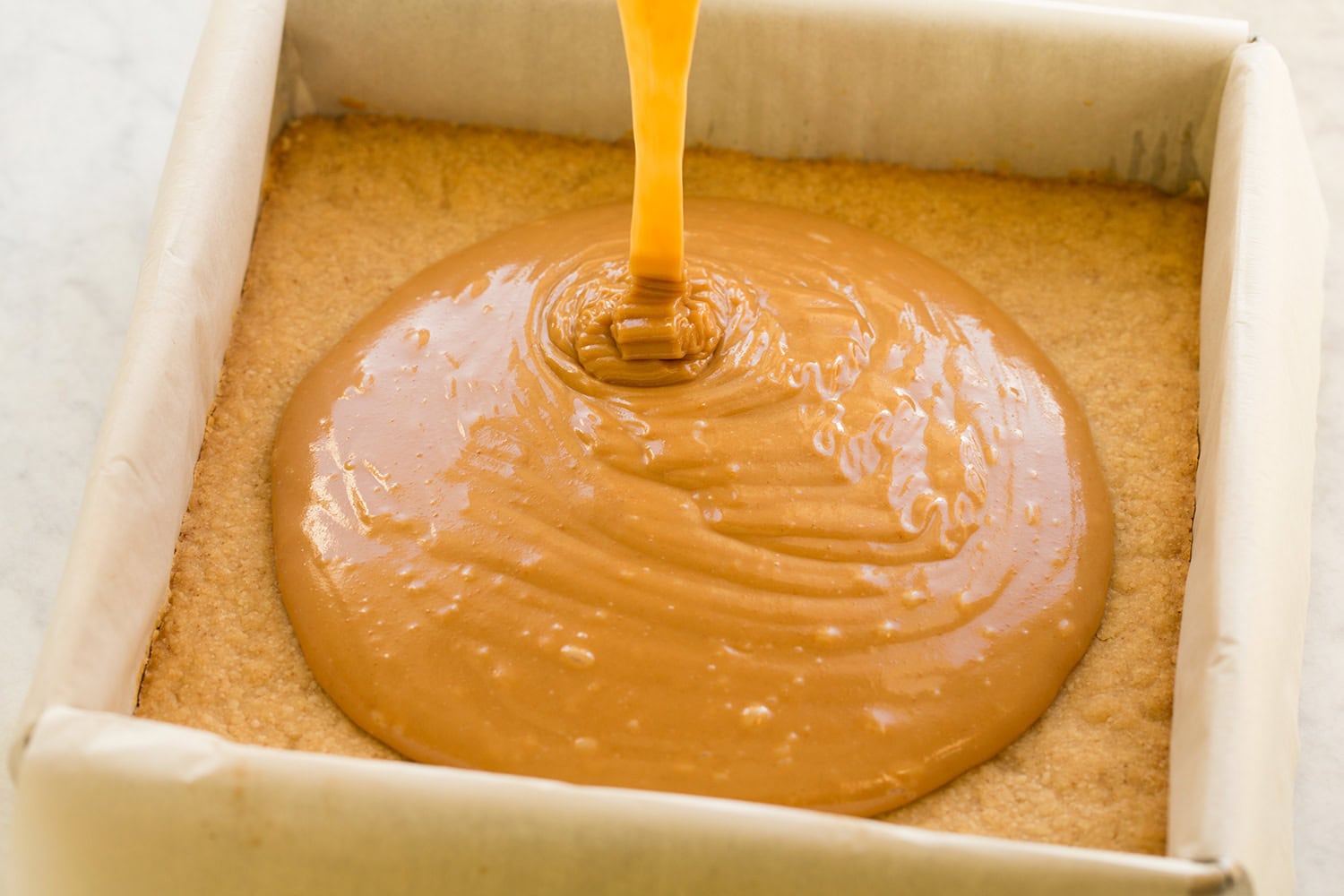 Caramel being poured over shortbread layer.
