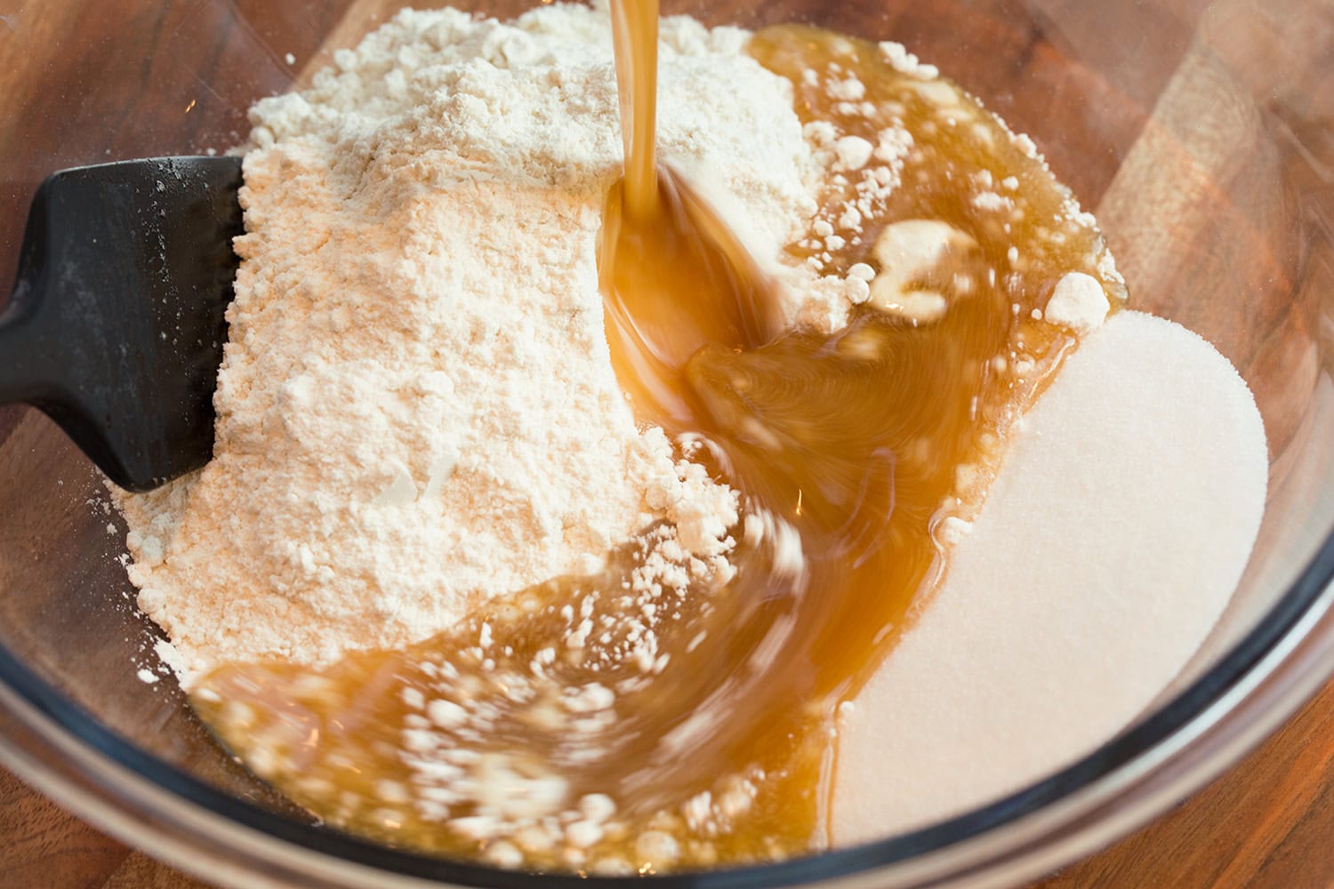 Browned butter being poured over sugar and flour in a mixing bowl.