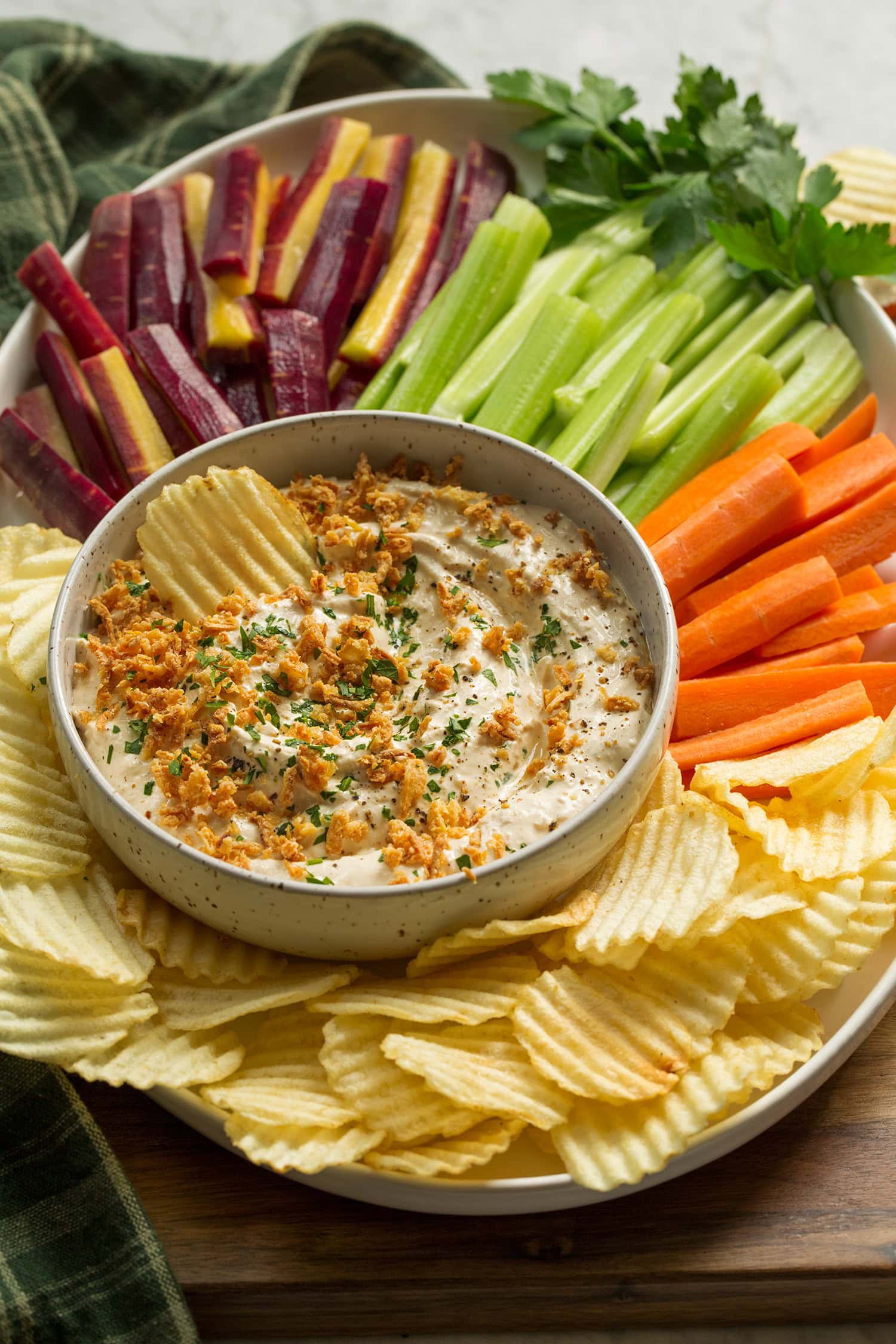 Homemade French onion dip in a bowl on a platter with carrots, celery and potato chips.