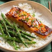 Close up of miso salmon garnished with green onions served over white rice with green beans on the side.