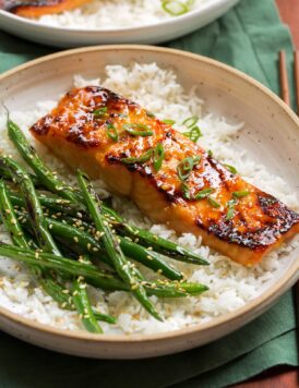 Close up of miso salmon garnished with green onions served over white rice with green beans on the side.