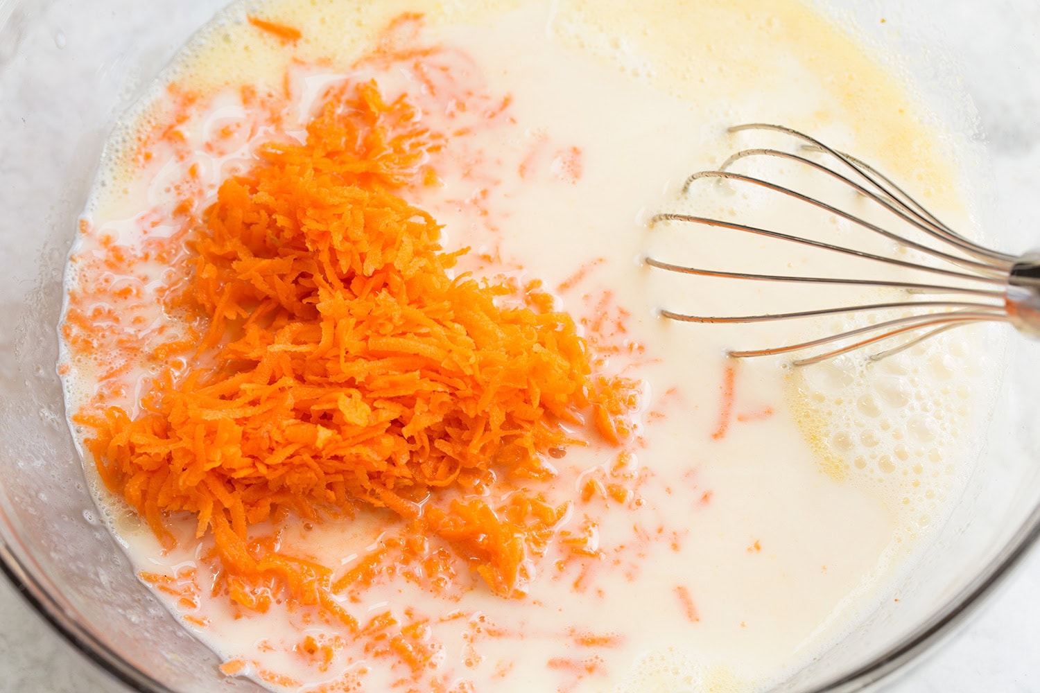 Fine shredded carrots and milk in glass dish.