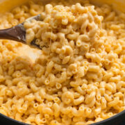 Close up photo of mac and cheese scooped out on a wooden spoon. Shows thick creamy texture of sauce and stringy cheese.