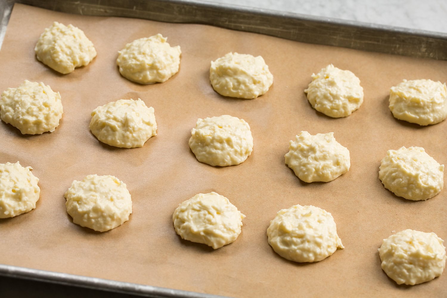 Brazilian Cheese Bread (Pão de Queijo) Rounds of the Brazilian cheese bread batter dropped onto a parchment paper lined baking sheet. Shown raw before baking.