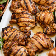Grilled chicken thighs with pretty black grill marks shown in a single layer on a platter with parsley to the side for garnish.