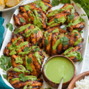 Grilled Peruvian chicken on a white platter, chicken is drizzled in aji verde sauce a Peruvian green cilantro sauce.