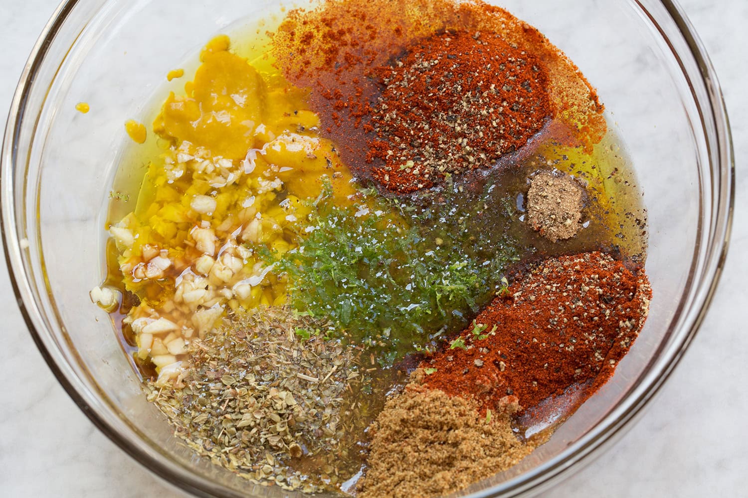 Peruvian chicken marinade ingredients, spices, seasonings, oil, lime, aji amarillo shown in a glass mixing bowl before mixing.
