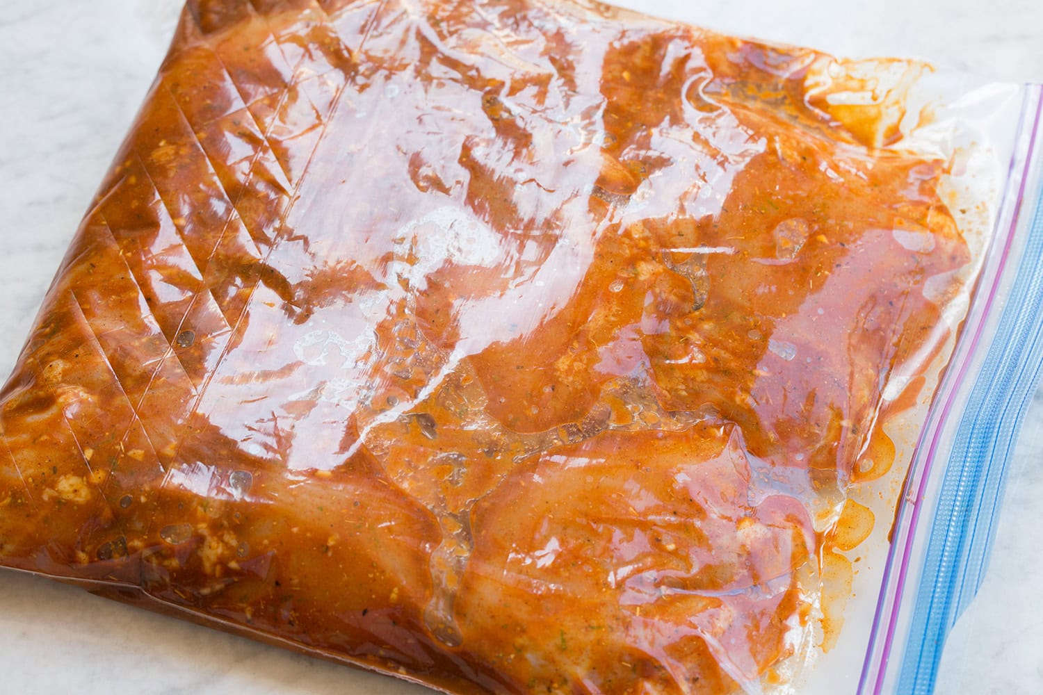 Chicken thighs soaking in Peruvian chicken marinade in a large resealable bag.