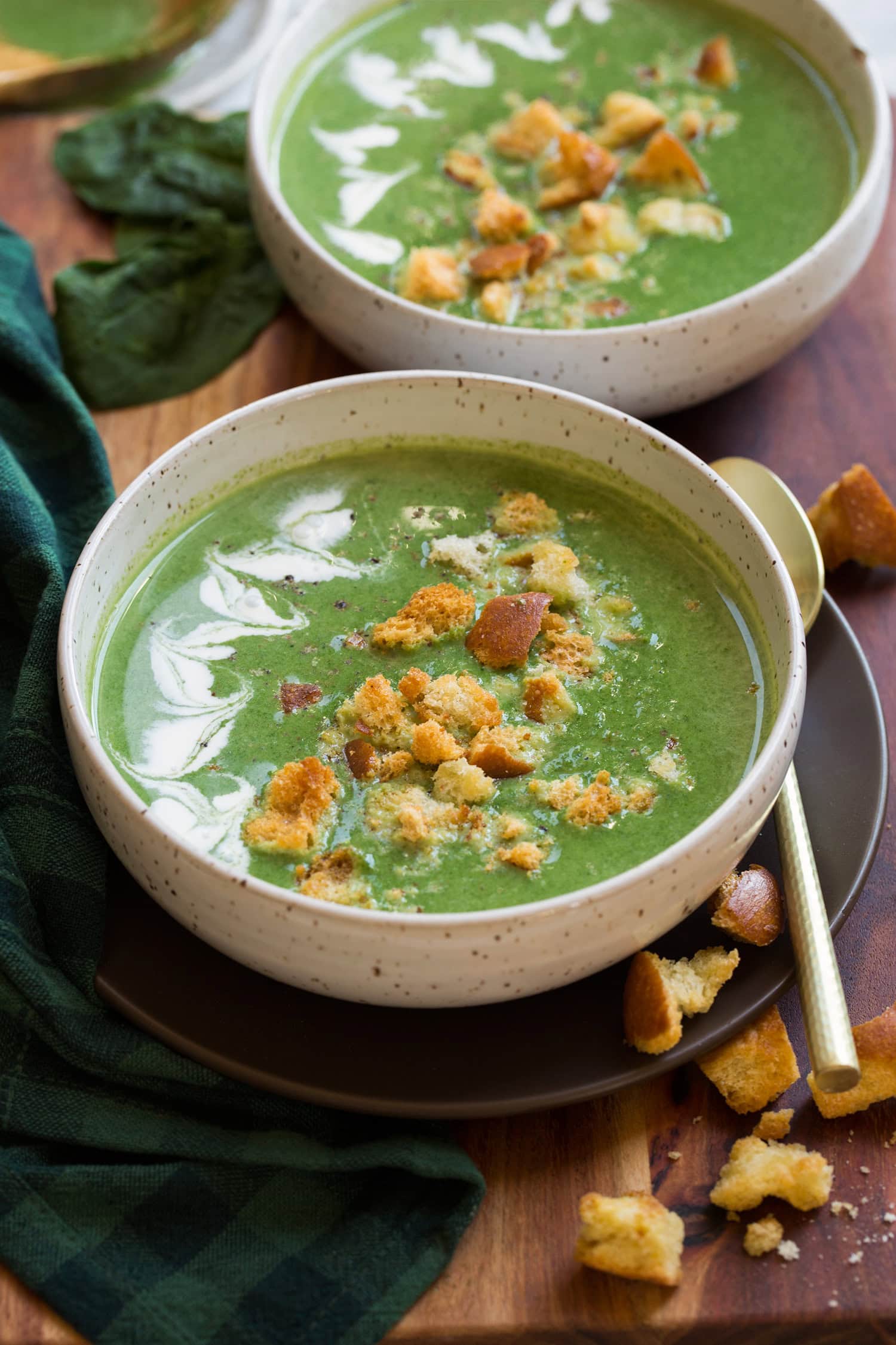 Spinach soup shown with cream, homemade croutons and parmesan cheese on top. Two servings shown in white bowls.