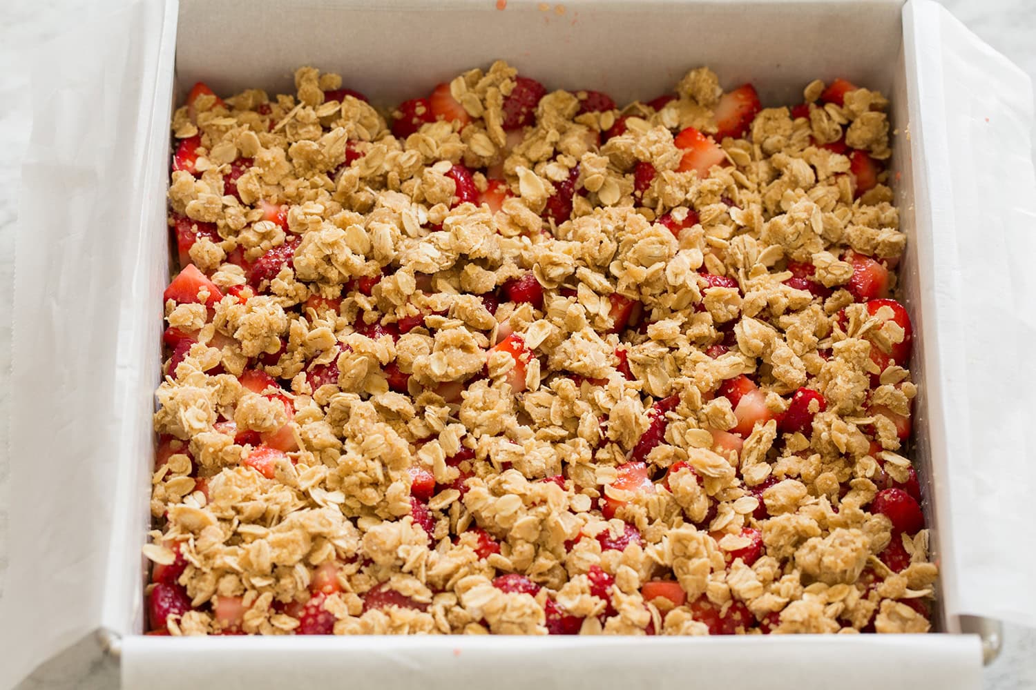 Oatmeal crumb topping added over strawberry layer in baking dish, shown before baking.