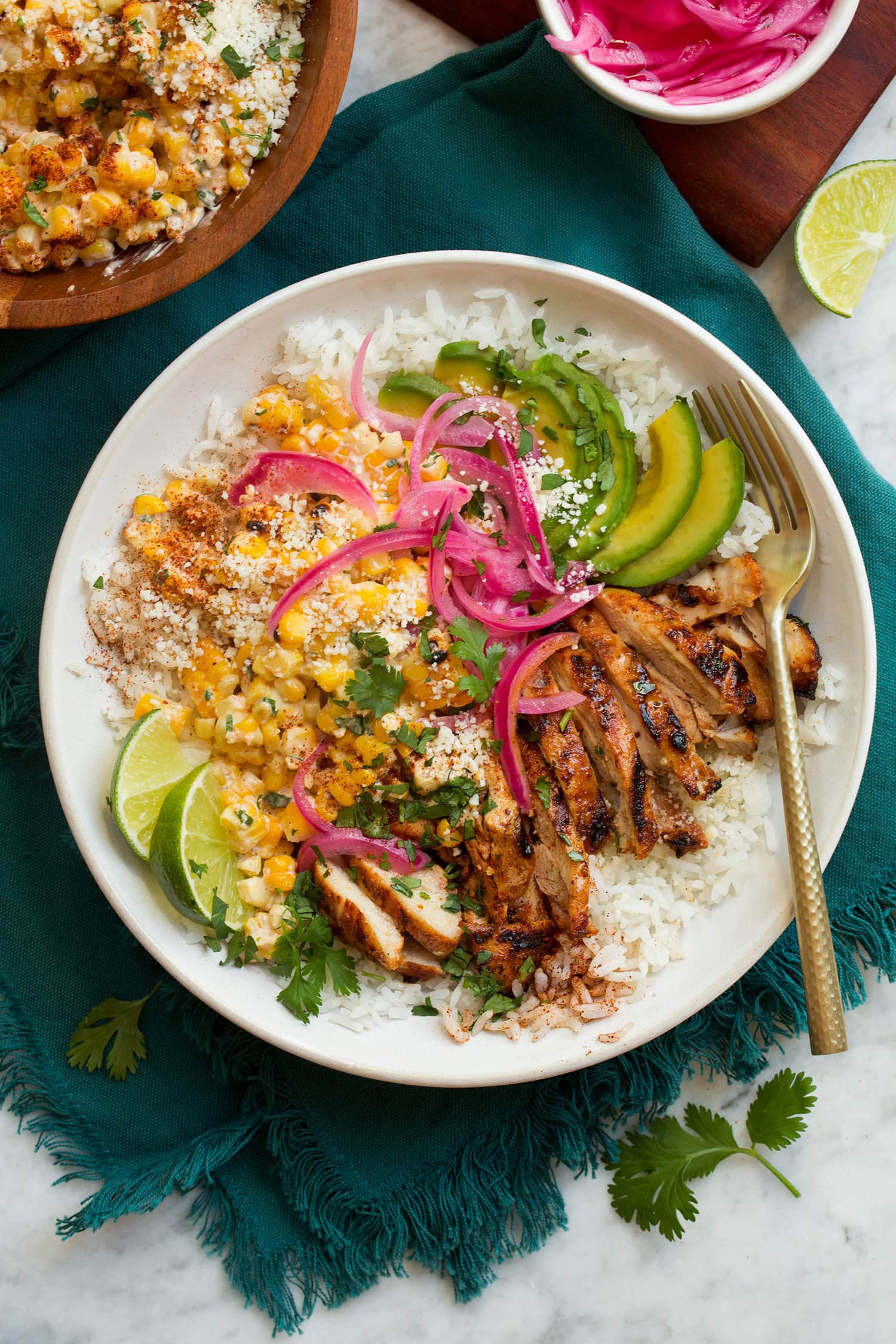 Street Corn Chicken Rice Bowl Overhead image of street corn and chicken rice bowl on a blue cloth on a marble surface.