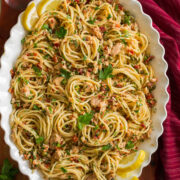 Overhead photo of tuna pasta made with spaghetti noodles, canned tuna, capers, and sun dried tomatoes in a scalloped white bowl.