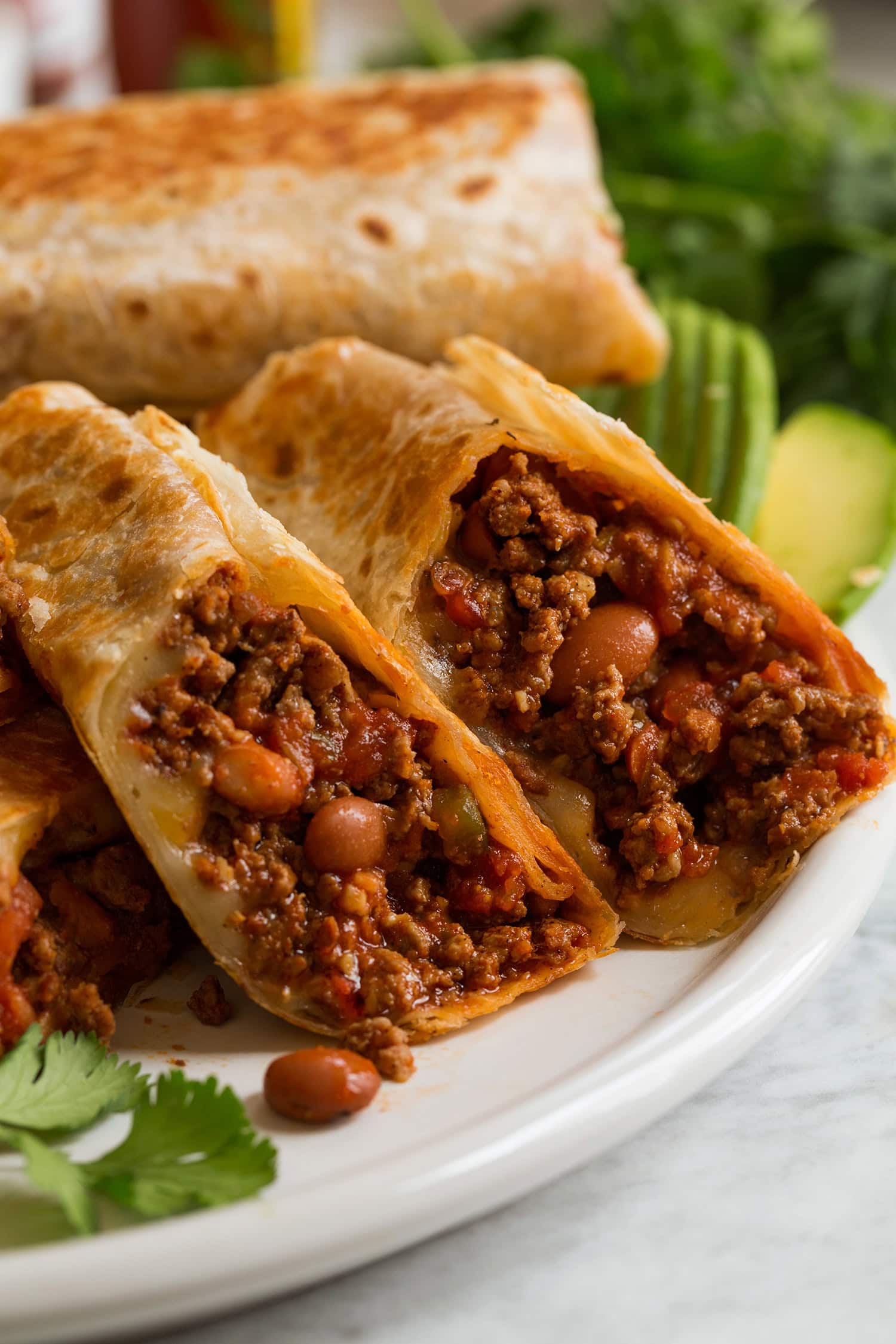 Easy Ground Beef Burritos Close up photo of ground beef and bean burritos with cheese, sliced in half exposing filling.