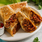 Easy homemade ground beef burritos shown aligned on a platter and cut into halves to show filling.