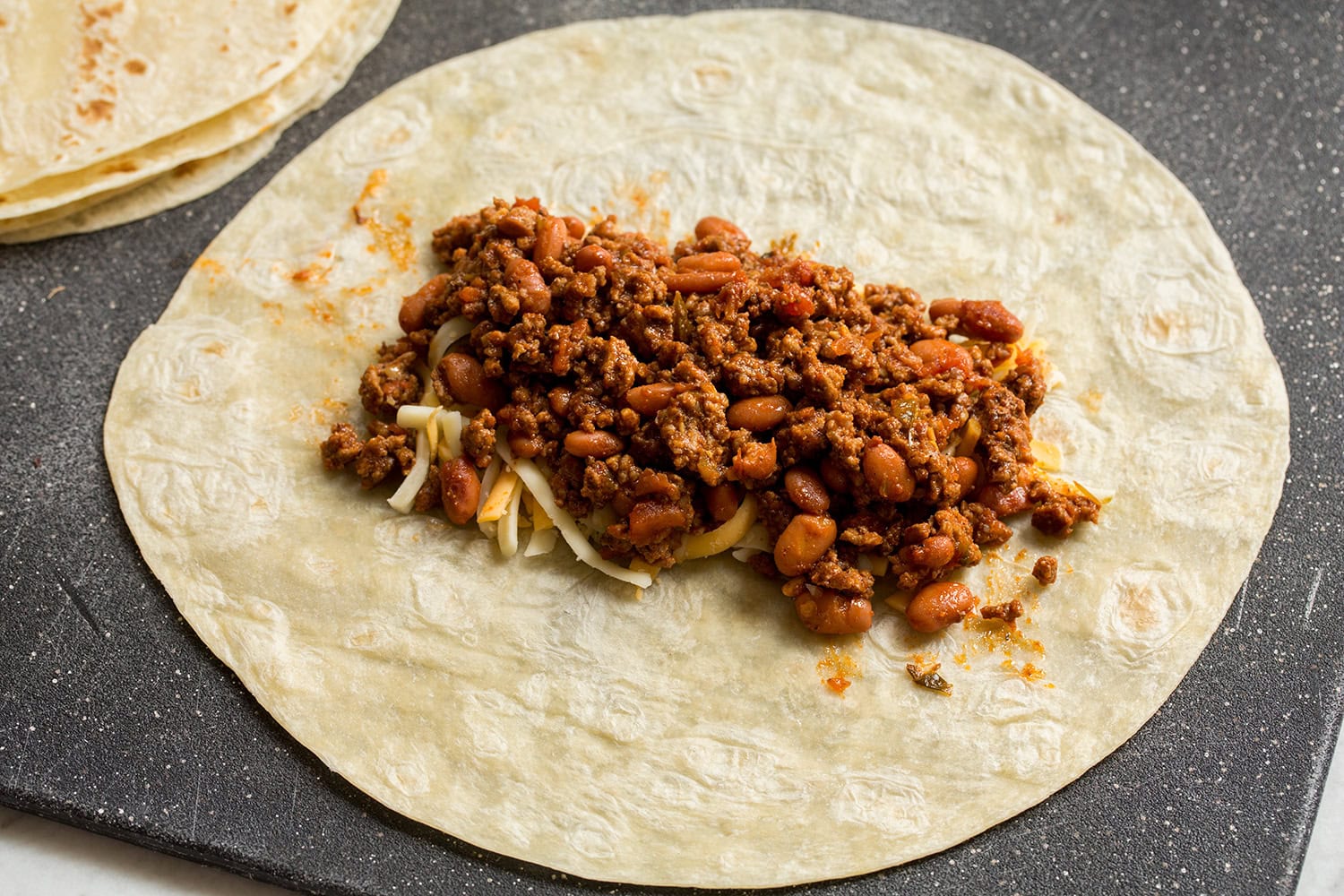 Easy Beef Burritos Assembling beef filling added over cheese layer on tortillas.