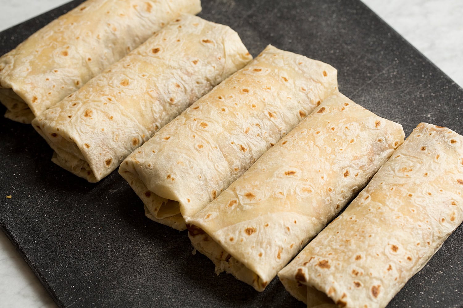 Easy Beef Burritos Five assembled burritos shown on a prep board.
