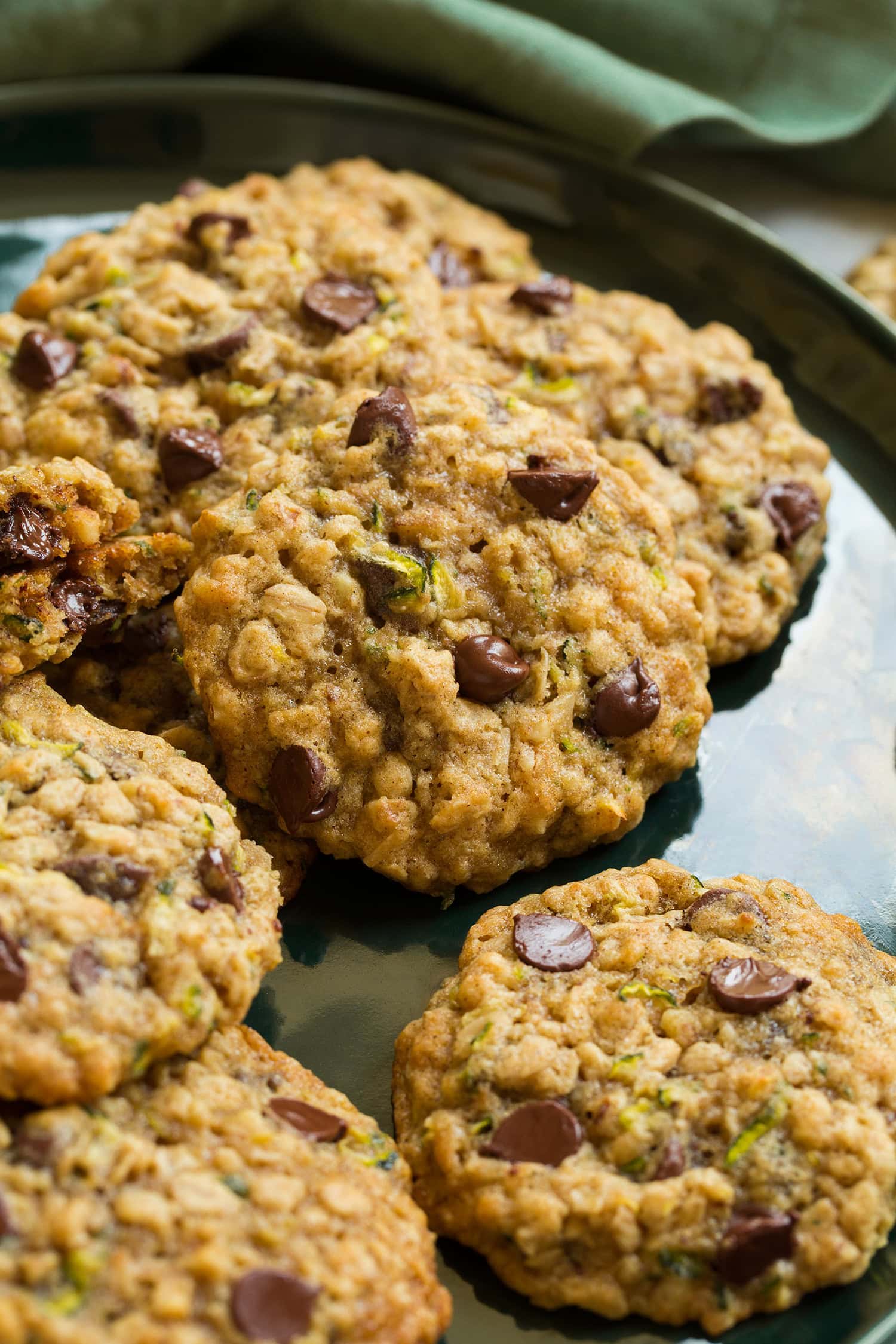 Close up photo of zucchini oatmeal cookies with chocolate chips on a green plate with a green cloth in the background.